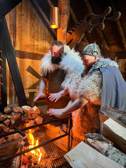 two strong Viking men warm their hands at a campfire